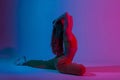 Pretty beautiful young woman in a stylish wear doing fitness in the studio with a bright neon light. Athletic attractive girl