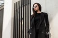 Pretty beautiful young woman in trendy sunglasses in cool black youth clothes with stylish handbag is resting near vintage Royalty Free Stock Photo