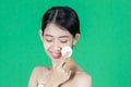 Pretty beauty young Asian woman cleaning her face with cotton pad over green isolated background. Healthy skin and cosmetics Royalty Free Stock Photo