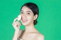 Pretty beauty young Asian woman cleaning her face with cotton pad over green isolated background. Healthy skin and cosmetics Royalty Free Stock Photo