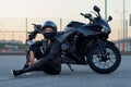 Biker woman in black leather jacket and full face helmet sits near stylish sports motorcycle at urban parking. Traveling Royalty Free Stock Photo