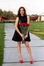 Pretty birthday girl with brown hair in little black dress posing, smiling and holding a bouquet of red roses Royalty Free Stock Photo