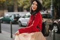 Pretty black-haired girl with shy smile plays with skirt on the street with cars on background. Outdoor portrait of glad Royalty Free Stock Photo