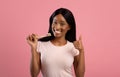 Pretty black lady with beautiful smile holding wooden toothbrush and showing thumb up gesture on pink background Royalty Free Stock Photo
