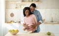 Pretty black pregnant woman cooking healthy breakfast in kitchen and her boyfriend hugging her from behind Royalty Free Stock Photo