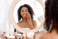 Pretty black woman looking in the mirror and applying facial moisturizer creme Royalty Free Stock Photo