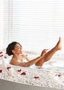 Pretty black young woman shaving legs while taking bath