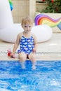 Pretty blond little girl wearing elegant blue swimsuit sitting near the pool in a beautiful sunny summer day Royalty Free Stock Photo