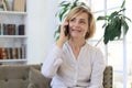 Pretty blond middle aged woman talking on mobile phone sitting on sofa Royalty Free Stock Photo