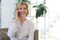 Pretty blond middle aged woman talking on mobile phone sitting on sofa Royalty Free Stock Photo