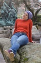 Pretty blond woman with knit cap sitting in a park on a rock