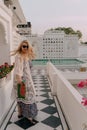 Pretty blond woman walks toward a swimming pool at a luxury palace resort, holding a handbag. Concept for luxury, vacation, wealth Royalty Free Stock Photo