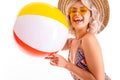 Pretty blonde caucasian female stands in swimsuit with big rubber beach colourful ball and smiles isolated on white