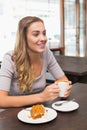 Woman in casual top holding white coffee mug while sitting at cafe table beside cake slice Royalty Free Stock Photo