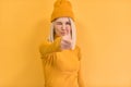 Pretty blonde female gives thumb up, approves new good idea, blink with the eye, wears yellow outfit, stands against yellow studio