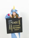 Pretty blonde girl with cozy blue unicorn costume with blackboard with different words on it like love and peace and some more