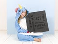 Pretty blonde girl with cozy blue unicorn costume with blackboard with different words on it like love and peace and some more