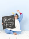 Pretty blonde girl with cozy blue unicorn costume with blackboard with different words on it like love and peace and some more