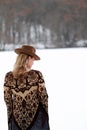 Blonde hippy woman with fringed patterned bohemian poncho outdoors in snow with wearing cowboy hat with feathers Stevie Nicks vibe