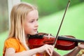 Pretty blonde little girl playing violin with a blurry green background Royalty Free Stock Photo