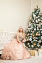Pretty blonde woman in beautiful holiday puffy elegant evening dress with makeup and curly hairstyle sitting posing on sofa near