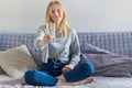 Pretty blonde woman drinking water and sitting on the sofa at home in the living room. Beautiful young girl with glass of water, Royalty Free Stock Photo