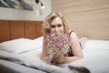 Pretty blonde woman have fine on her bed in bedroom with a bouquet of small flowers. Adult lady enjoying her morning and Royalty Free Stock Photo