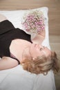 Pretty blonde woman have fine on her bed in bedroom with a bouquet of small flowers. Adult lady enjoying her morning and Royalty Free Stock Photo