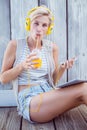 Pretty blonde woman listening music with her mobile phone and drinking orange juice Royalty Free Stock Photo