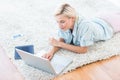 Pretty blonde woman lying on the floor and using her laptop Royalty Free Stock Photo