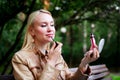 Pretty blonde woman paints her lips outdoors. Correcting make up Royalty Free Stock Photo