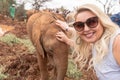 Pretty blonde woman pets a baby elephant in Nairobi Kenya