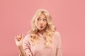 Pretty blonde woman stretching chewing gum from mouth and looking away at free space, pink studio background Royalty Free Stock Photo