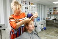 Pretty blonde working as a hairdresser and cutting hair tips of a female customer in a beauty salon. Woman visits the hairdresser Royalty Free Stock Photo