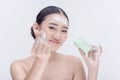 A pretty and blooming Asian girl holding a bar of facial soap while forming a finger heart sign.
