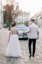 Pretty bride and handsome groom walking in the old city center, standing in front of the black retro car Royalty Free Stock Photo