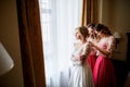 Pretty bridesmaids in pink dresses help bride to put on a wedding dress