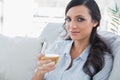 Pretty brunette drinking white wine sitting on sofa Royalty Free Stock Photo