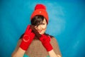 Pretty brunette girl wearing fashion red knitted winter gat and warm beautiful gloves on blue studio solid background Royalty Free Stock Photo