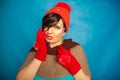 Pretty brunette girl wearing fashion red knitted winter gat and warm beautiful gloves on blue studio solid background Royalty Free Stock Photo