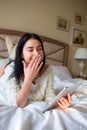 Pretty brunette girl in white knitted dress lying on bed with a tab in and hands and laughing covering her mouth with a hand Royalty Free Stock Photo