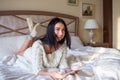 Pretty brunette girl in white knitted dress lying on bed with a tab in and hands and laughing covering her mouth with a hand Royalty Free Stock Photo