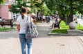 Pretty brunette girl or woman from behind in blue jeans, white shirt and grey knitted modern decorated bag, on city blurry