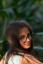 Pretty brunette with glasses looking with her head turned back, green plant background. Royalty Free Stock Photo