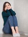 Pretty brunette woman with magnificent eyes and adorable smile in green sweater and blue jeans relaxing sitting on floor at home Royalty Free Stock Photo