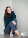 Pretty brunette woman with magnificent eyes and adorable smile in green sweater and blue jeans relaxing sitting on floor at home Royalty Free Stock Photo