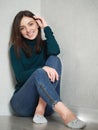 Pretty brunette woman with magnificent eyes and adorable smile in green sweater and blue jeans relaxing sitting on floor at home Royalty Free Stock Photo