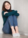 Pretty brunette woman with magnificent eyes and adorable smile in green sweater and blue jeans relaxing sitting on floor hugging Royalty Free Stock Photo