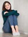 Pretty brunette woman with magnificent eyes and adorable smile in green sweater and blue jeans relaxing sitting on floor hugging Royalty Free Stock Photo