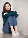 Pretty brunette woman with magnificent eyes and adorable smile in green sweater and blue jeans relaxing sitting on floor hugging Royalty Free Stock Photo